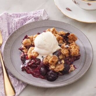 Close-up of berry crisp on a small serving plate topped with ice cream, with more ice cream on the side.