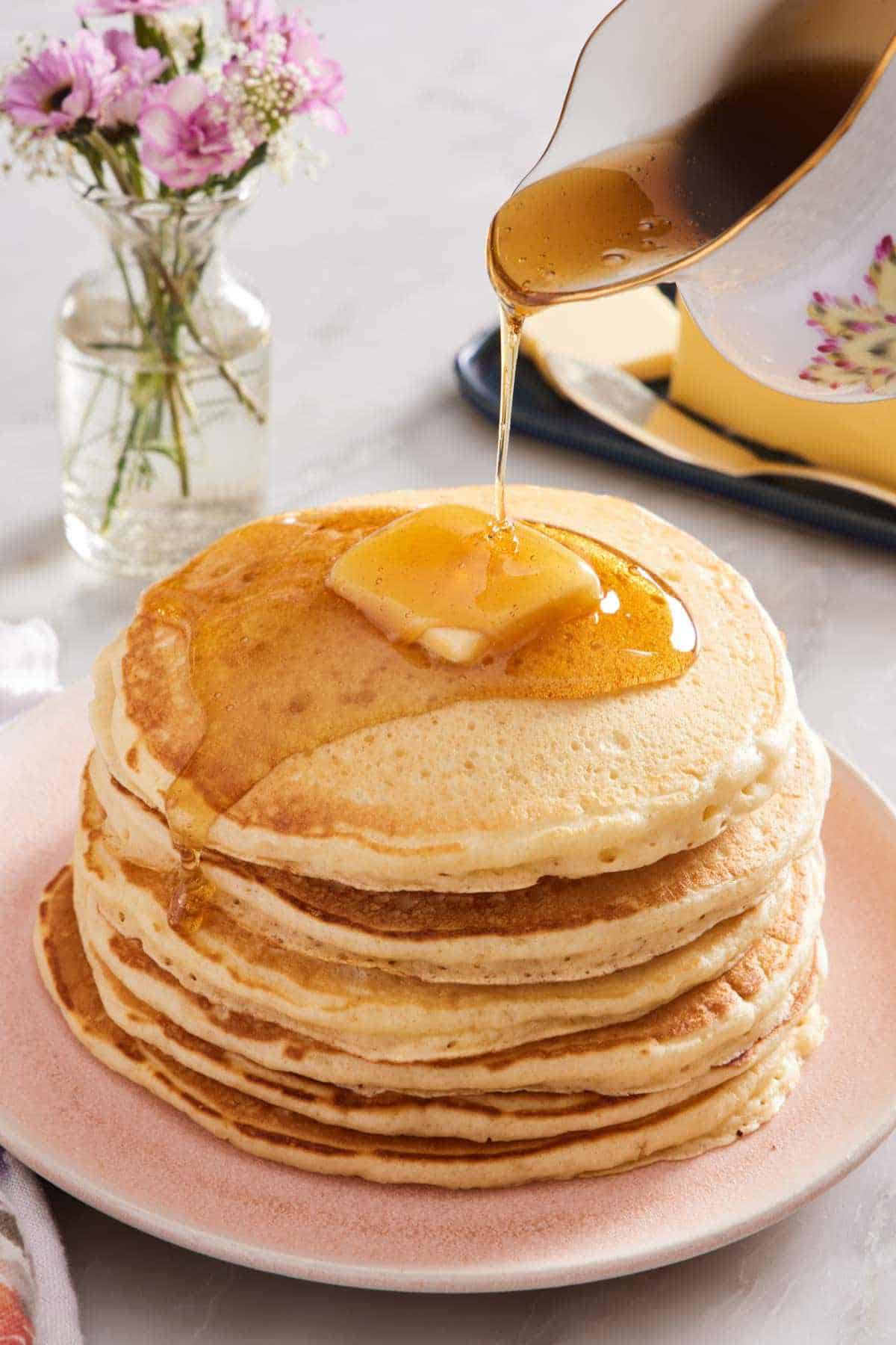 A stack of buttermilk pancakes with a pat of butter, drizzled with maple syrup.