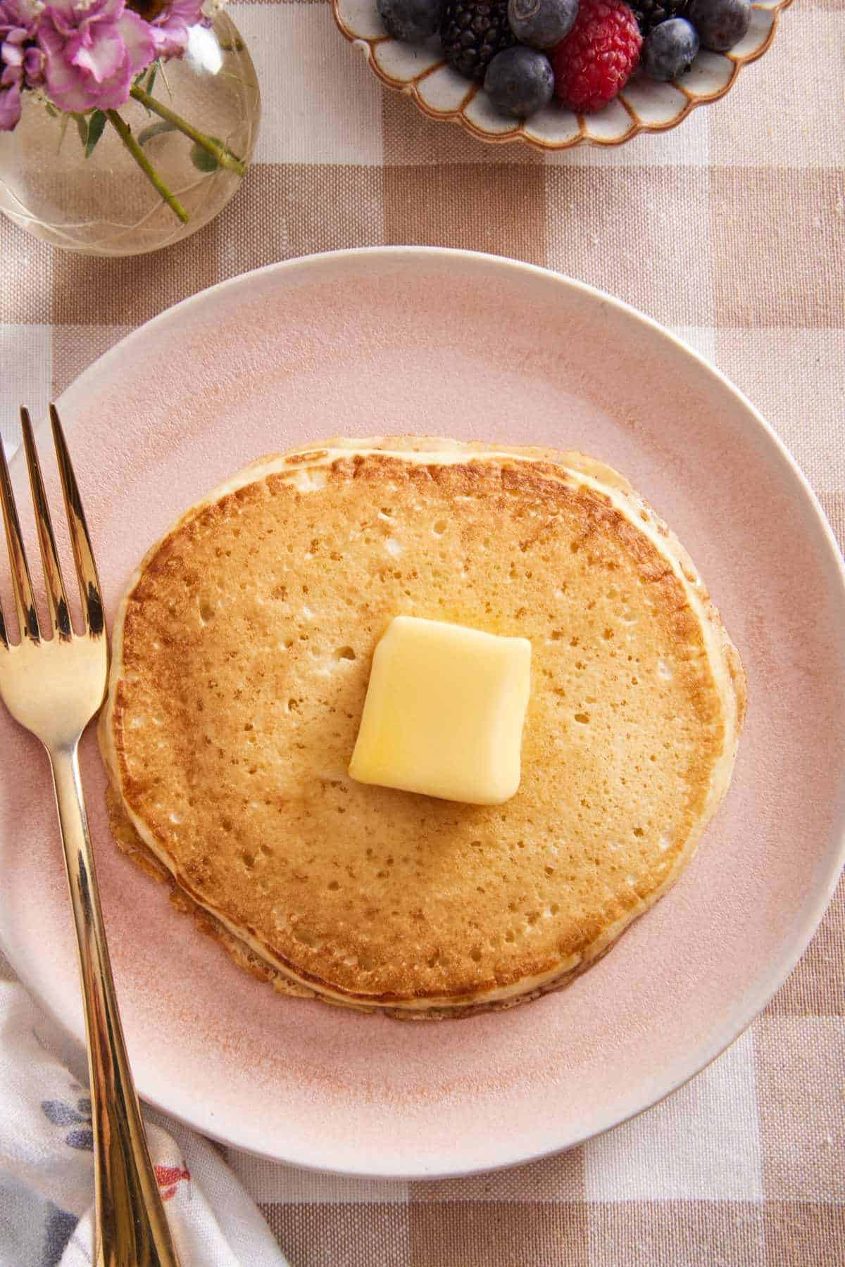 Overhead shot of a buttermilk pancake, topped with a pat of butter, on a plate with a fork.