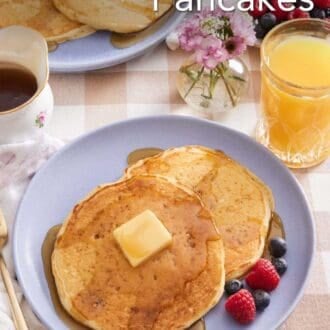 Pinterest graphic showing pancakes, topped with butter and maple syrup, on a plate with orange juice, a vase of flowers, and syrup on the side.