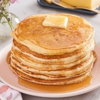 A stack of pancakes topped with butter and syrup with a fork on the side.