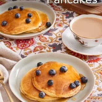 Pinterest graphic showing two plates of pancakes drizzled with maple syrup and topped with blueberries, with a cup of tea on the side.