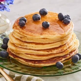 Close-up of a stack of cottage cheese pancakes drizzled with maple syrup and topped with blueberries.