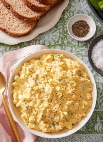 Egg-mayo salad in a large serving bowl with sliced of bread, salt, and pepper on the side.
