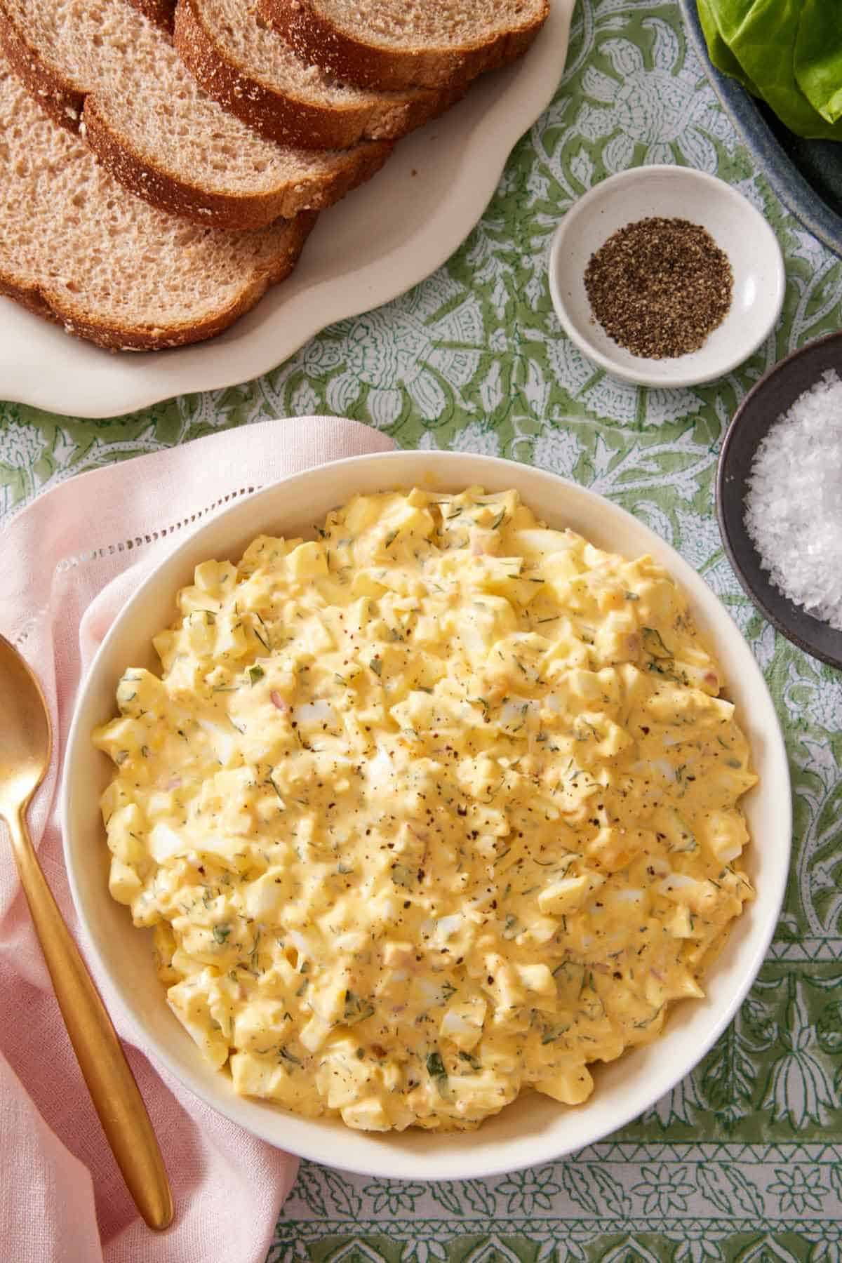 Egg-mayo salad in a large serving bowl with sliced of bread, salt, and pepper on the side.
