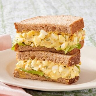 Egg salad sandwich with lettuce on a white plate.