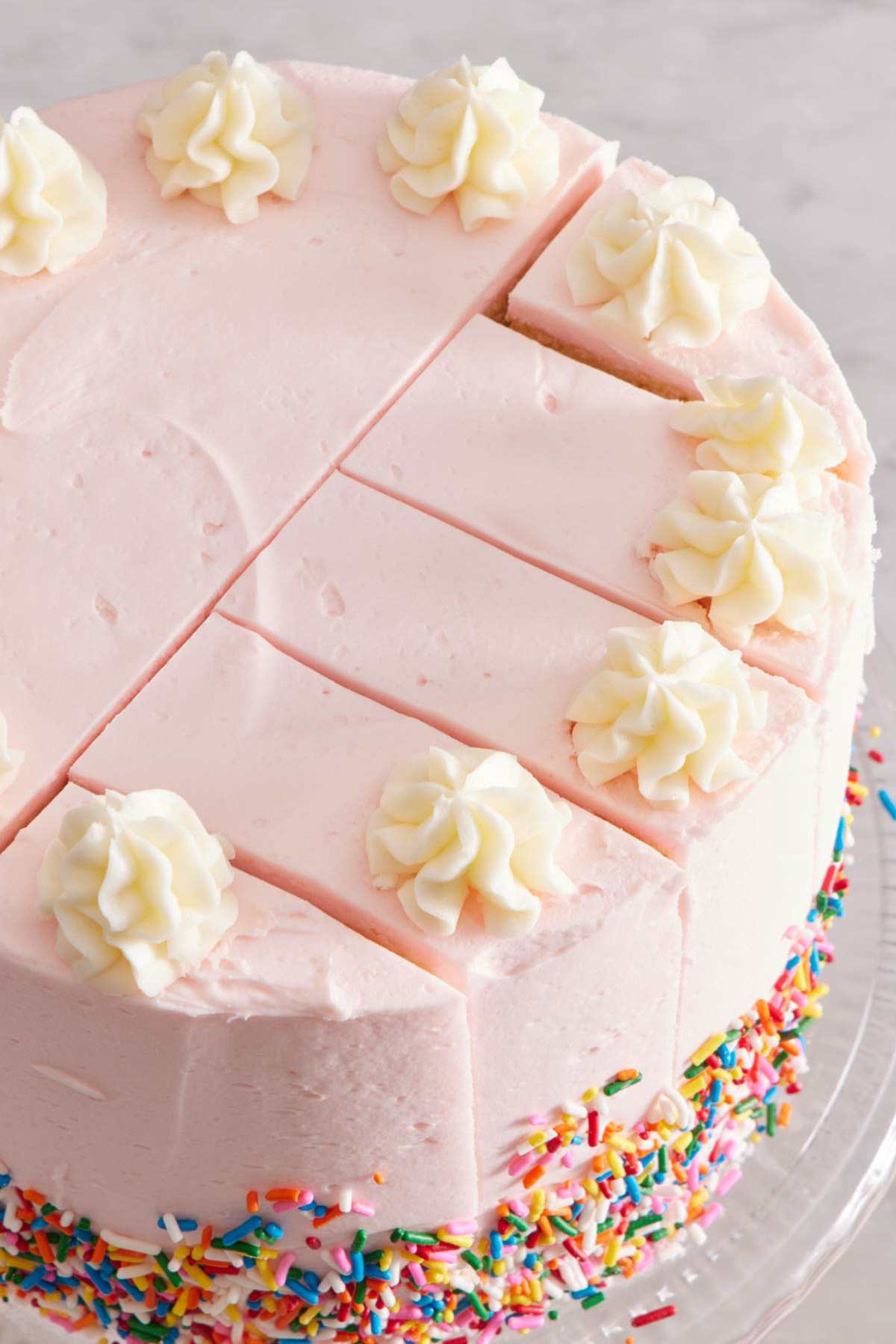 Image showing how to cut a round cake with one slice down the center and four perpendicular cuts to make five slices on a cake with pink frosting and sprinkles.