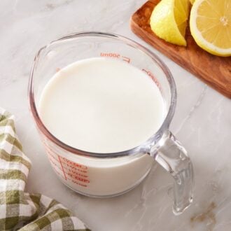 Buttermilk substitute in a glass measuring jug with a sliced lemon on a wooden cutting board next to it.