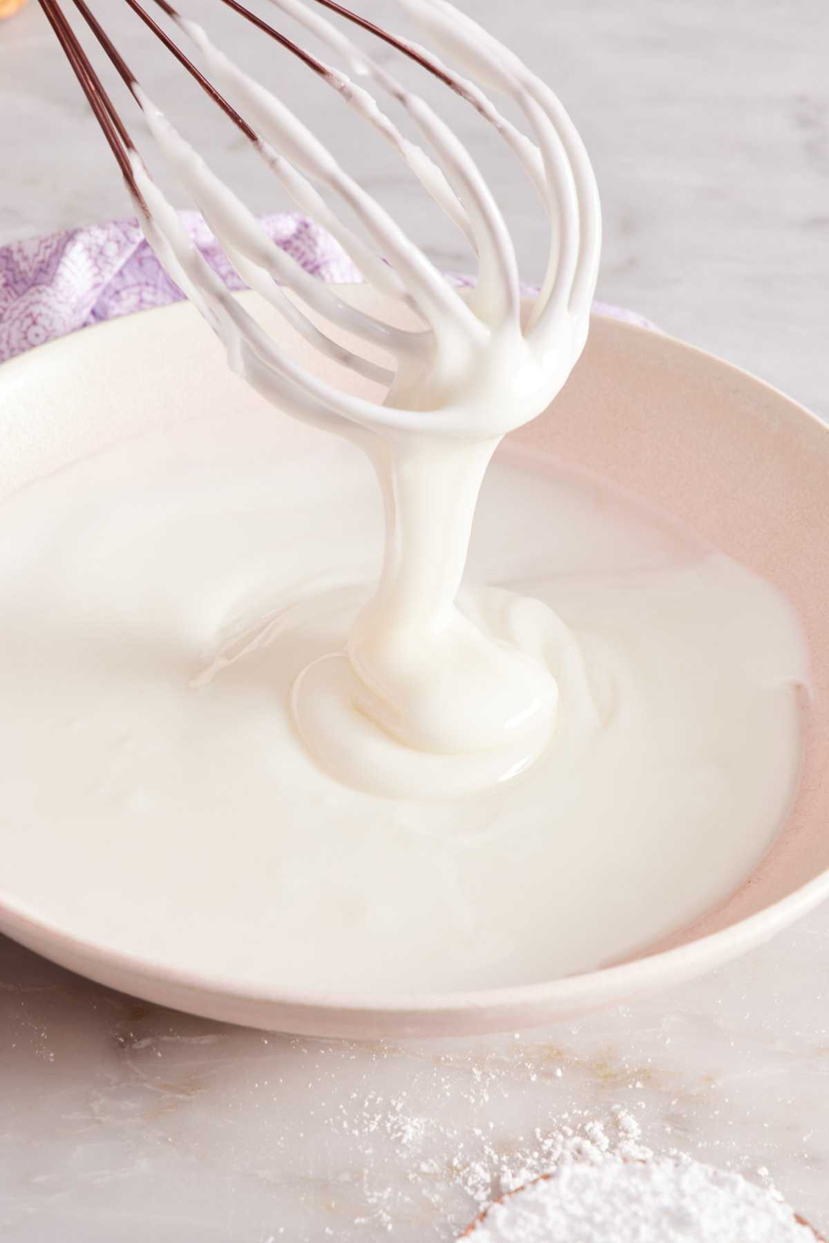 Lemon glaze in a bowl with a whisk showing its drizzling consistency.