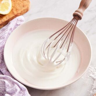 Lemon glaze in a bowl with a whisk with lemon wedges on a board, a measuring cup with powdered sugar, and a purple dishcloth around it.