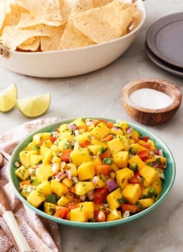 Homemade salsa in a serving bowl with tortilla chips in a bowl in the background. Salt and limes around the bowl.