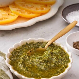 Pinterest graphic showing a basil and pine nut sauce in a white bowl with tomatoes and burrata cheese in the background.