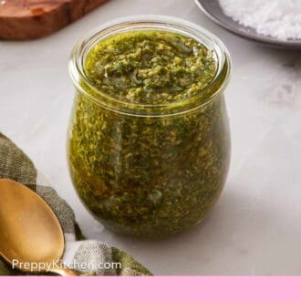 Pinterest graphic showing a glass jar containing a savory green sauce composed of basil, garlic, cheese, and olive oil.