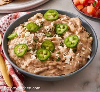 Pinterest graphic showing refried beans with toppings in a bowl with pico de gallo in the background.