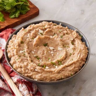 Beans in a bowl with a spoon next to it, with cheese and fresh cilantro on the side.