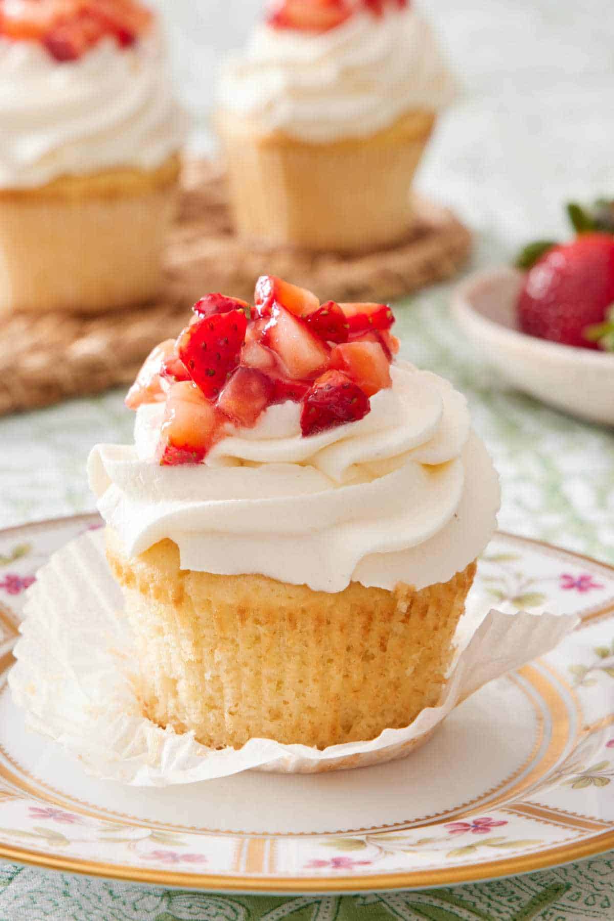 Strawberry shortcake cupcake on a plate topped with whipped topping and diced strawberries.