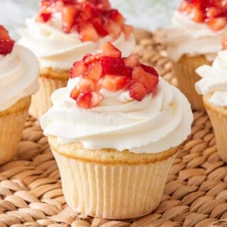 Five strawberry shortcake cupcakes on a woven serving platter.
