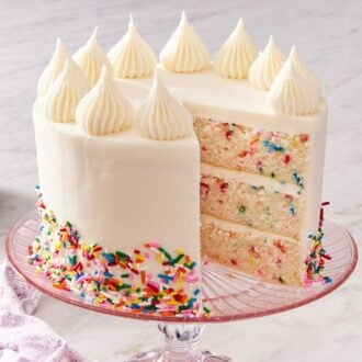 Funfetti cake on a pink cake stand with a slice cut out.