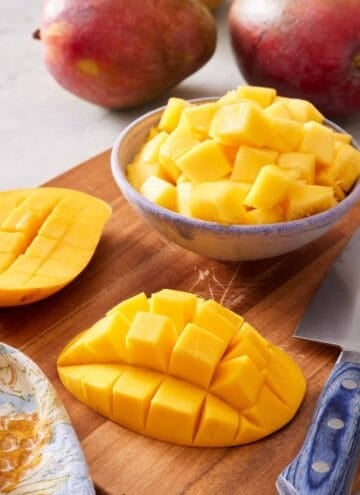 Mango cheeks with a grid cut into them, and cubed mango in a bowl. Whole mangoes in the background.