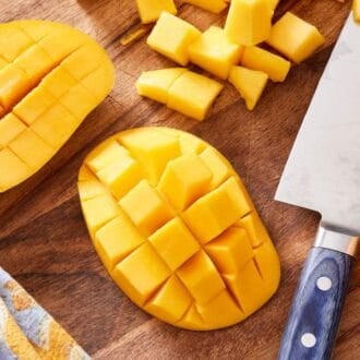 Image showing stages for how to cut a mango. There are cubes pieces, a large cheek with a grid scored in, and the skin turned inside out so the flesh is sticking out.