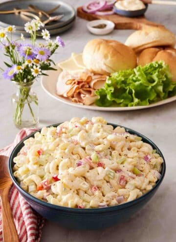 Macaroni pasta salad in a blue bowl with sandwich ingredients in the background.