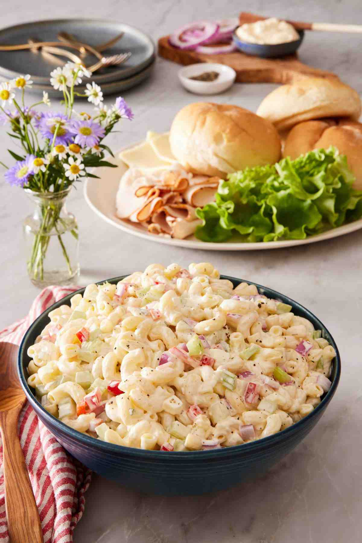 Macaroni pasta salad in a blue bowl with sandwich ingredients in the background.