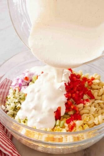 Creamy dressing poured over macaroni salad ingredients.