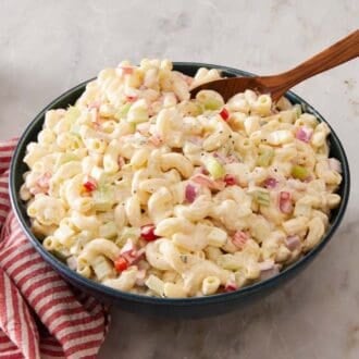 Macaroni salad in a blue bowl with a wooden serving spoon. A striped cloth is next to the bowl.