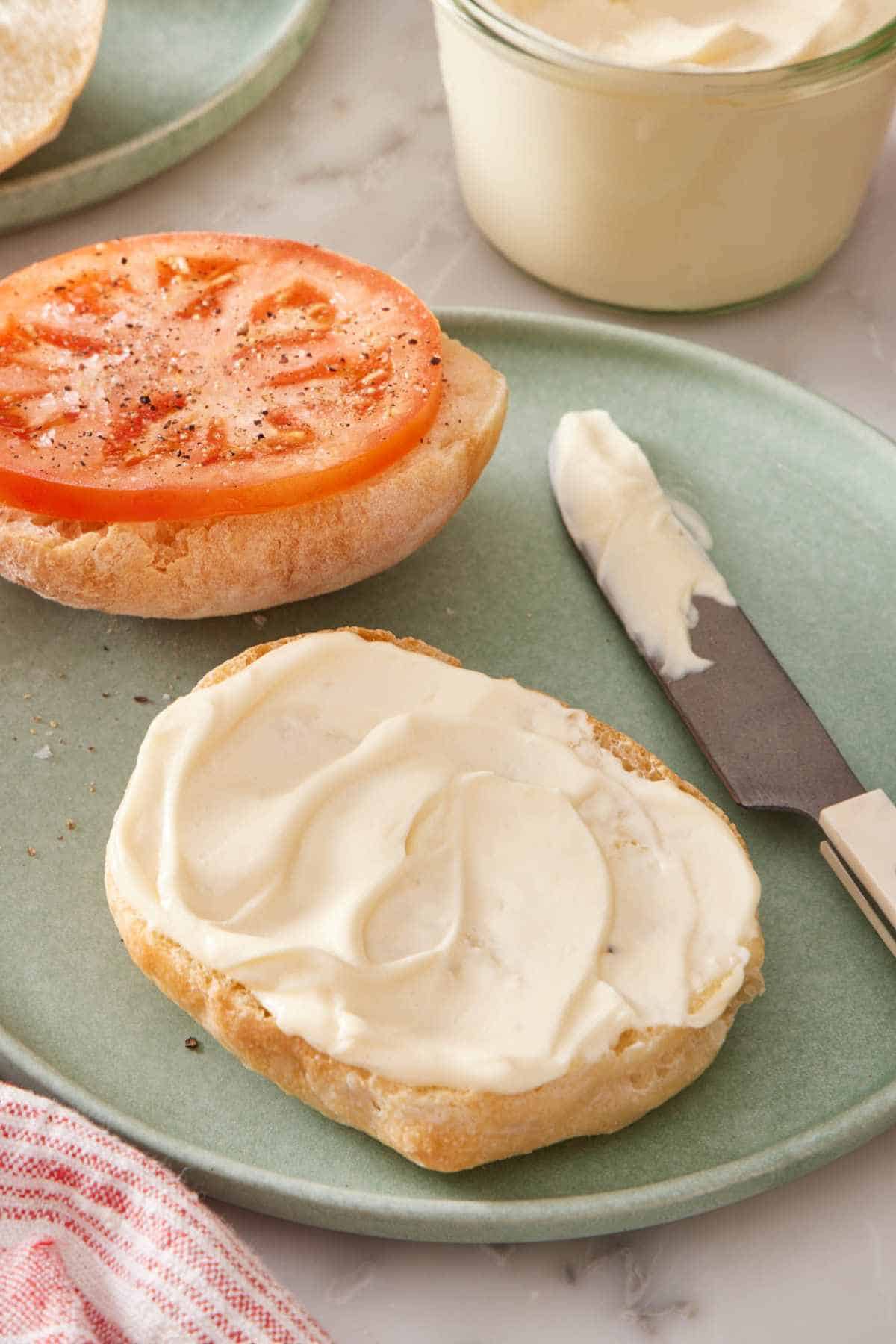 Homemade mayonnaise smeared on half a bun with a tomato slice on the other half.