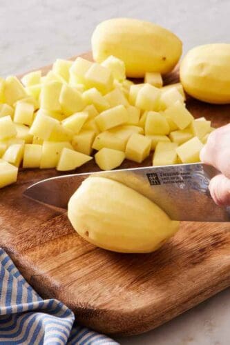 Potatoes cut into cubes on a wooden cutting board.