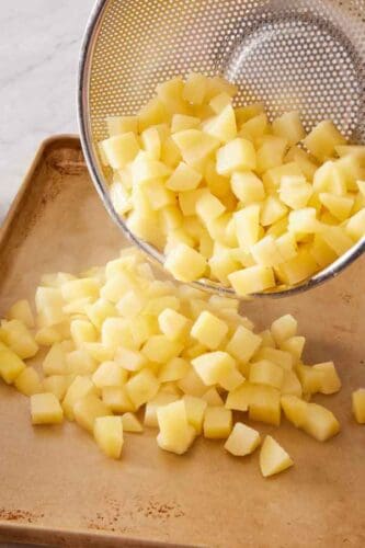 Boiled potatoes spread onto a baking tray to cool.