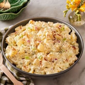 Close up of creamy potato salad with a checkered green and white linen alongside, with a wooden spoon resting on top.