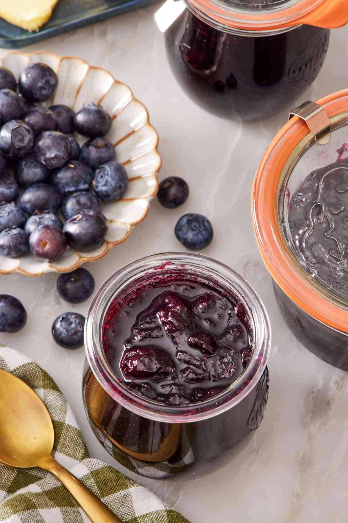 Overhead shot of a small jar of blueberry jam and a small bowl of fresh blueberries alongside.
