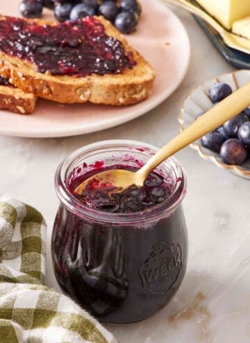 Close up of a small jar of homemade jam with toast and jam in the background.