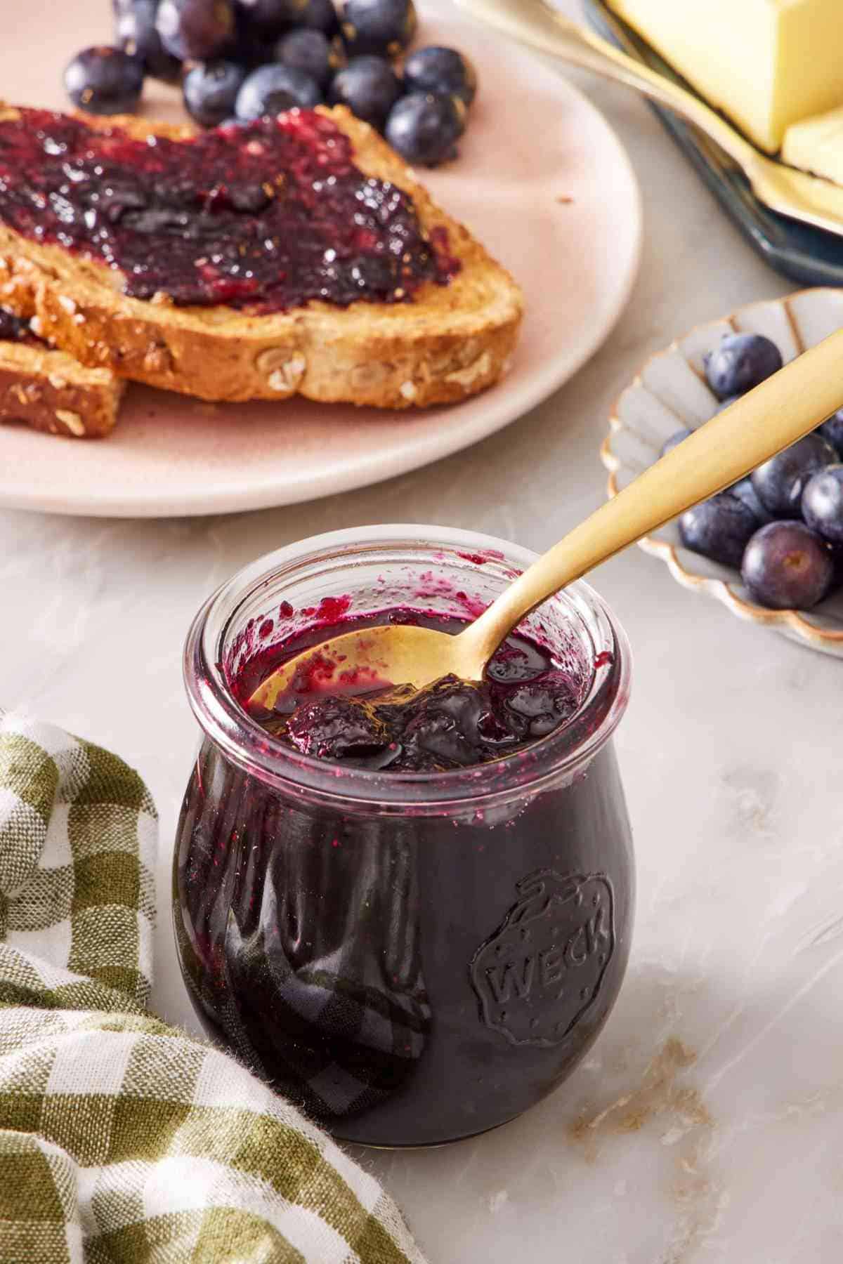 Close up of a small jar of homemade jam with toast and jam in the background.