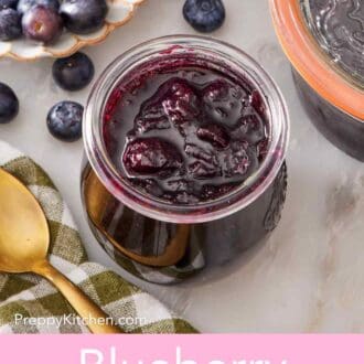 Pin image showing an overhead shot of homemade jam in a small jar with fresh blueberries in the background.