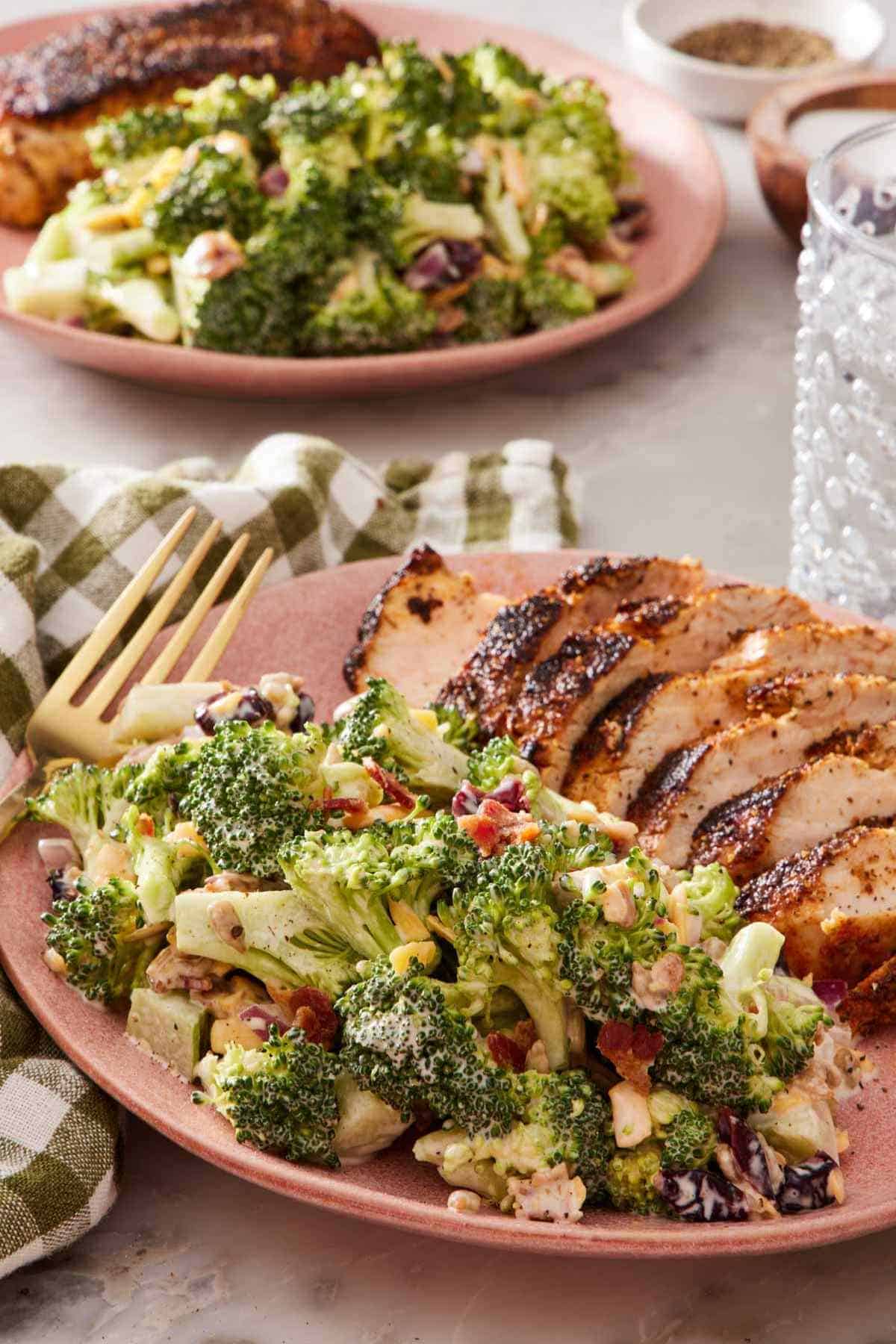 Broccoli salad on a plate with a sliced chicken breast. Another serving of the meal is in the background.