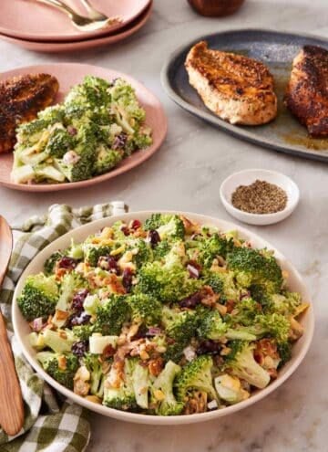 Broccoli salad in a bowl with more salad and cooked chicken breasts in the background.