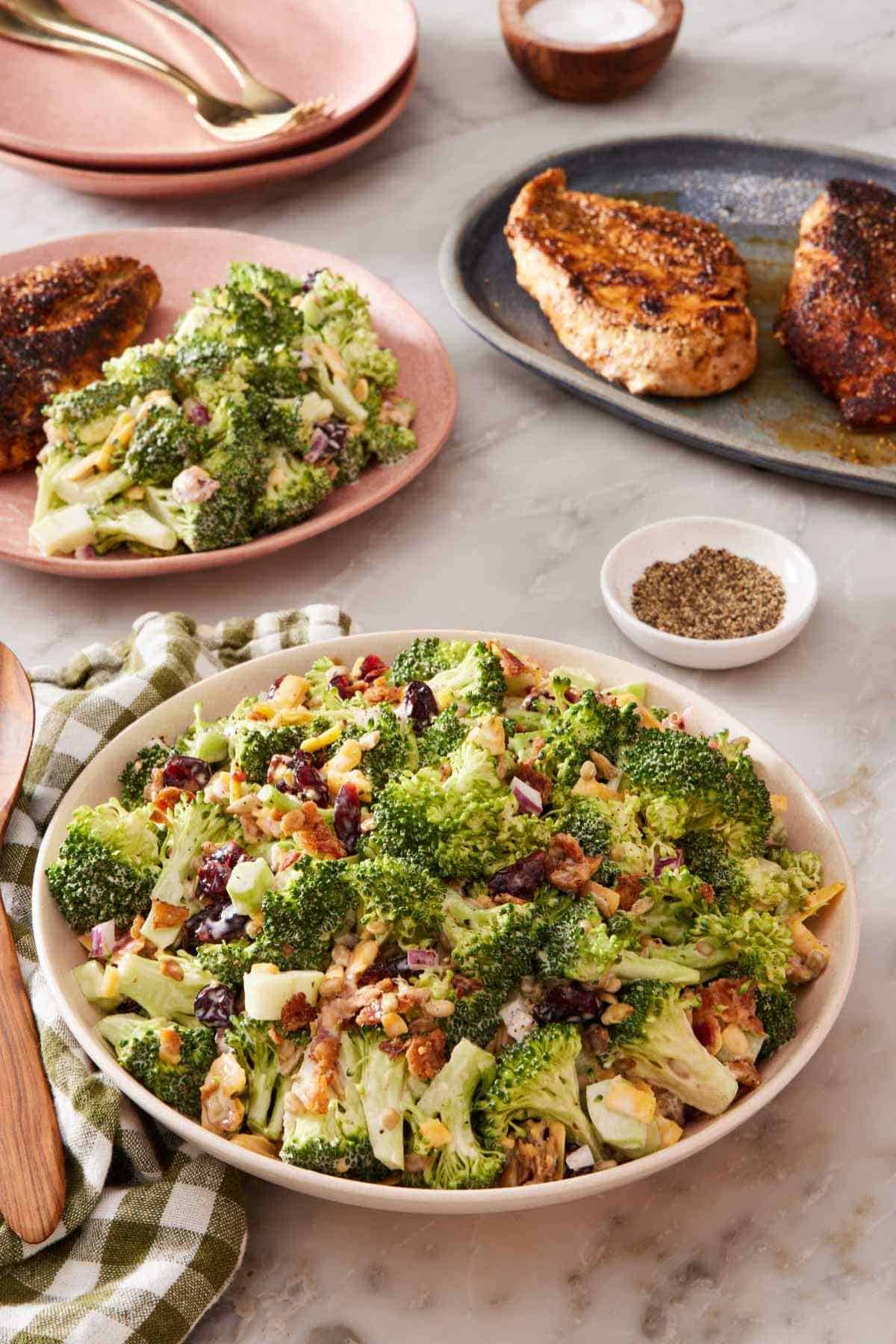 Broccoli salad in a bowl with more salad and cooked chicken breasts in the background.