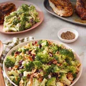 Pinterest graphic showing easy broccoli salad in a bowl with a green and white table linen next to it. Pepper, cooked chicken breasts, and a plate with salad and chicken in the background.
