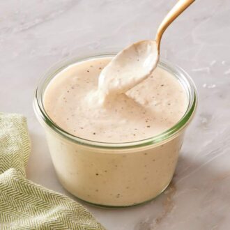 A small jar of creamy salad dressing with grated parmesan cheese and black pepper on the side.