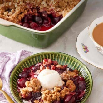 Pinterest graphic showing cherry crisp in a textured green bowl with a scoop of ice cream. A cup of tea is next to it and a casserole dish in the background.