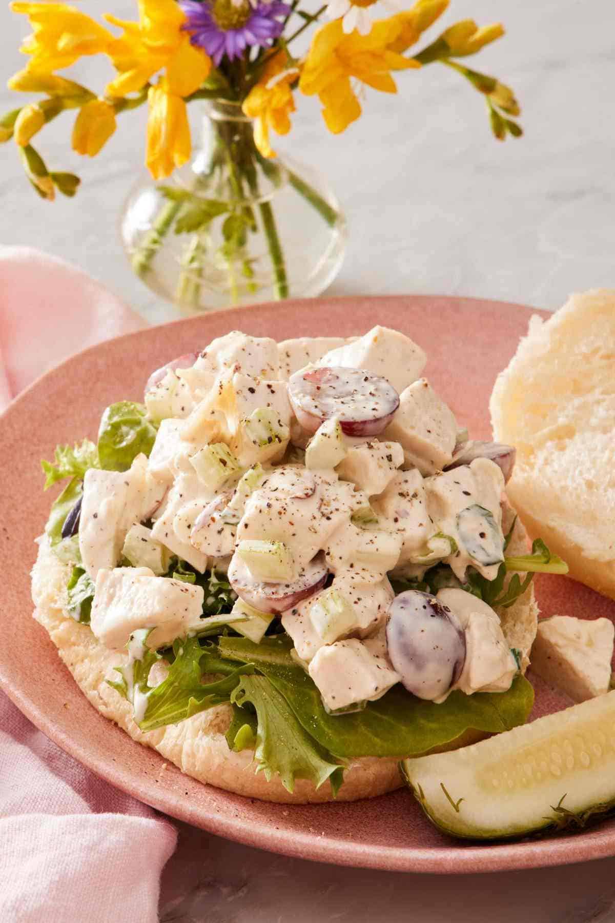 Chicken salad sandwich with the top bun and a sliced pickle on the side.