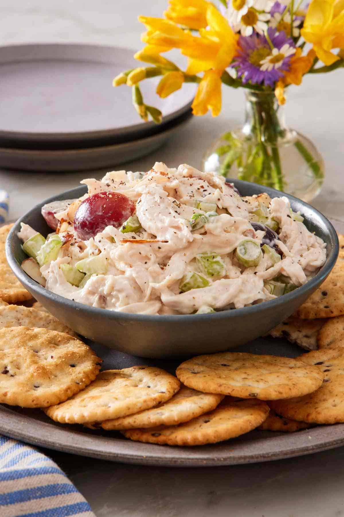 Chicken salad in a bowl placed on a plate filled with crackers.