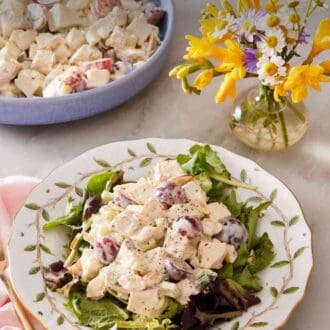 Pinterest graphic showing chicken salad on a plate served over mixed greens with a vase of flowers on the side.