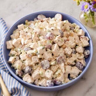 Chicken salad in a shallow bowl with a striped blue table linen, a fork, and black pepper on the side.