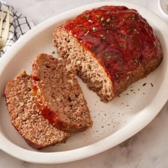 Sliced meatloaf on a serving dish with salt and pepper alongside.