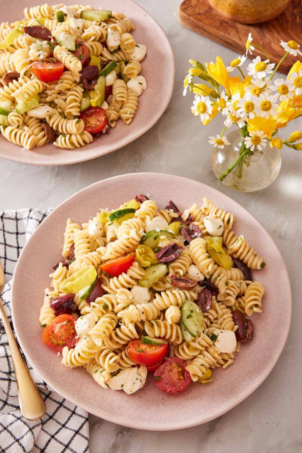 Two plates of homemade pasta salad with a small vase of flowers next to them.