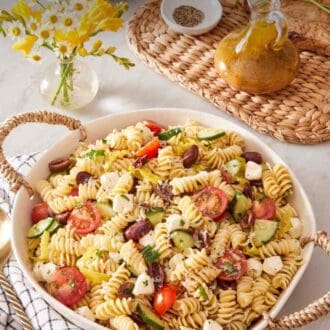 Pin image showing a dish of rotini salad with a dish linen alongside, with dressing, a vase of flowers, and black pepper in the background.