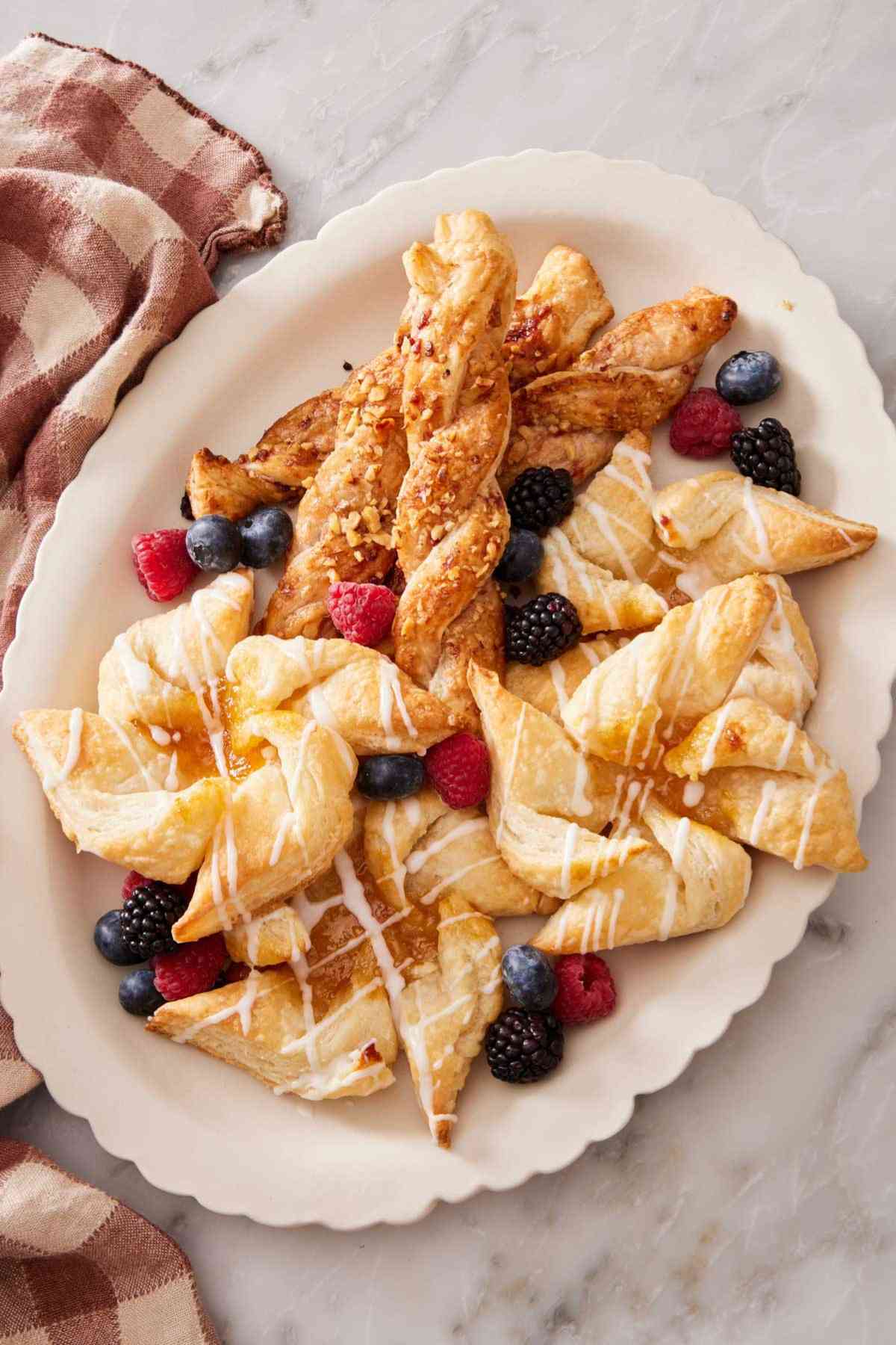 Puff pastry used in two different ways, as twists and as a Danish, on a large platter with fresh berries scattered on top.